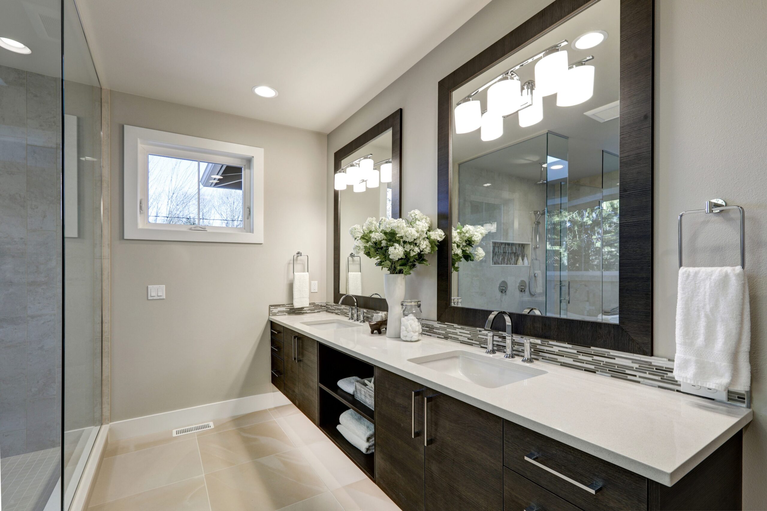 Modern coastal bathroom with mosaic tile wall, double vanity, gold fixtures, and warm lighting.