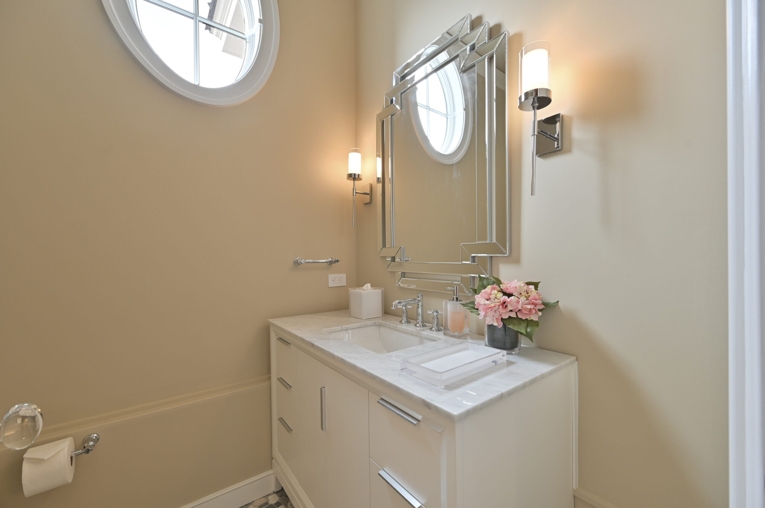 Modern bathroom vanity with marble countertop, geometric mirror, and pink flowers on the sink area